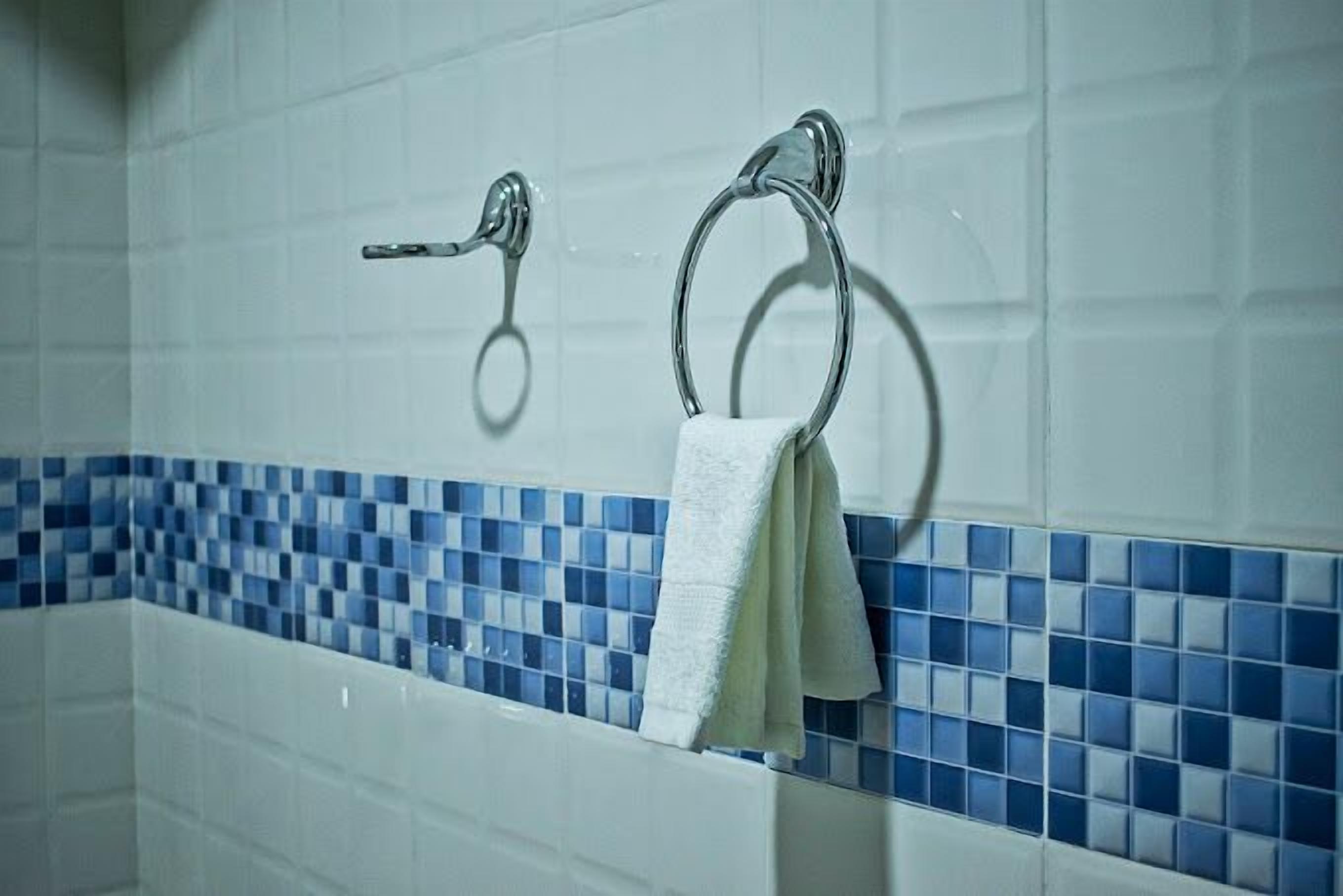 A bathroom with a white bathtub, blue mosaic tiles, and two towel rings.