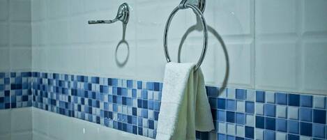 A bathroom with a white bathtub, blue mosaic tiles, and two towel rings.