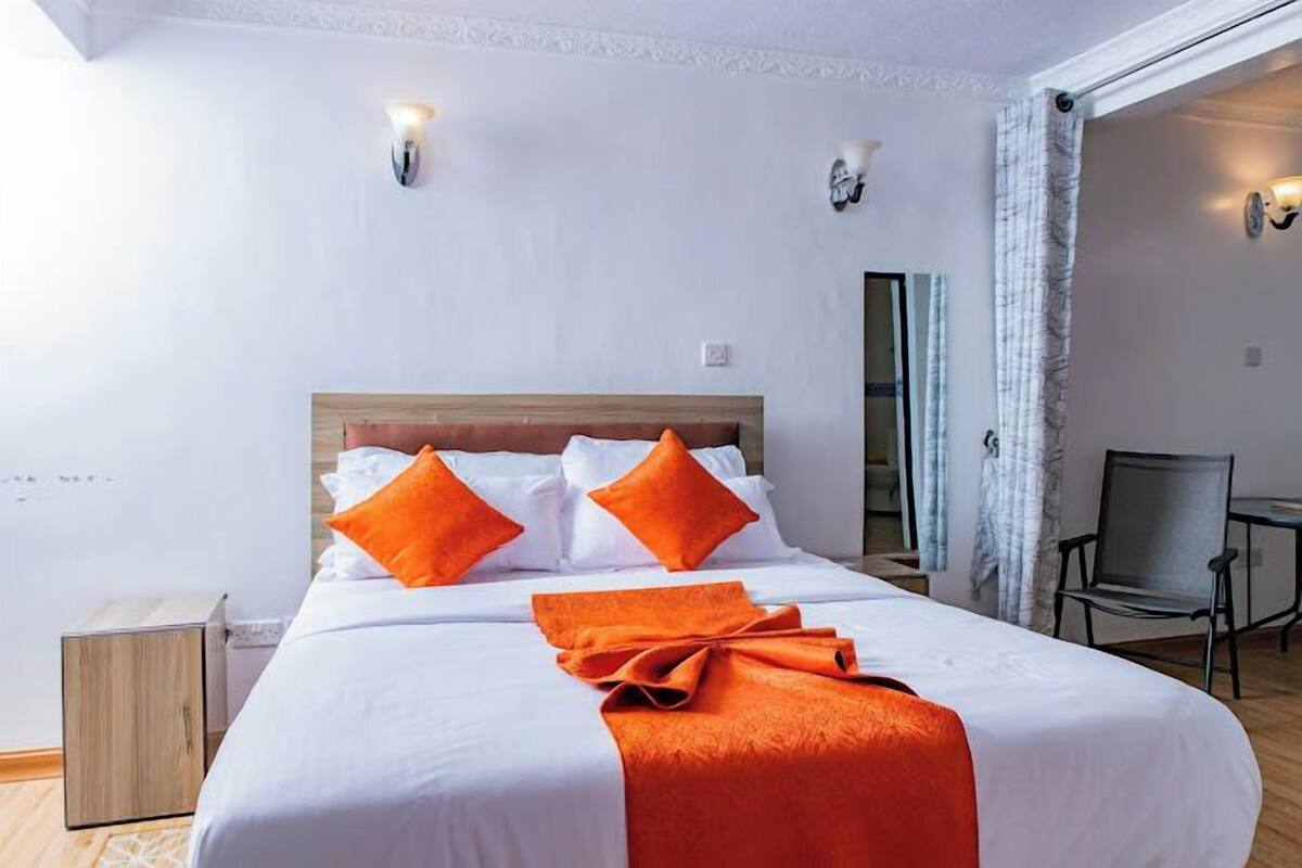 A hotel room with a bed, two wall sconces, a chair, and a mirror.