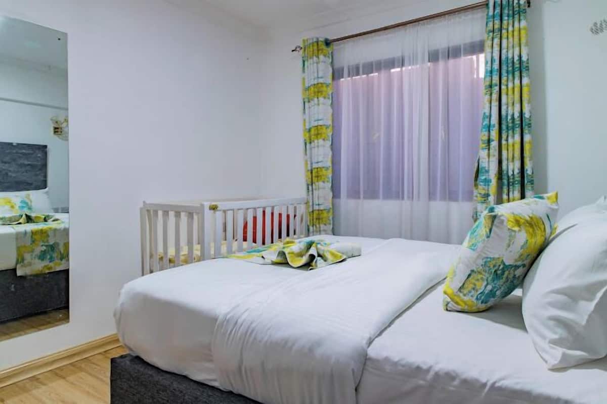 A bedroom with a bed, a crib, a mirror, and a window with curtains.