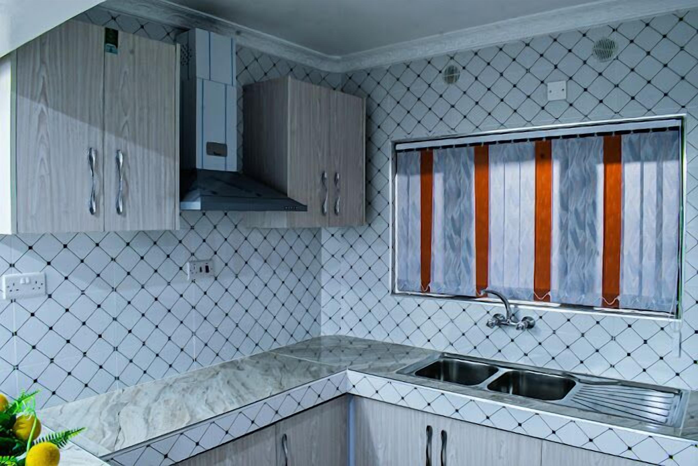 Una cocina compacta con encimera de mármol, pileta doble y muebles de madera.