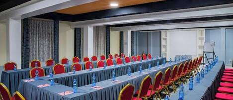A conference room with long tables, red chairs, and water bottles.