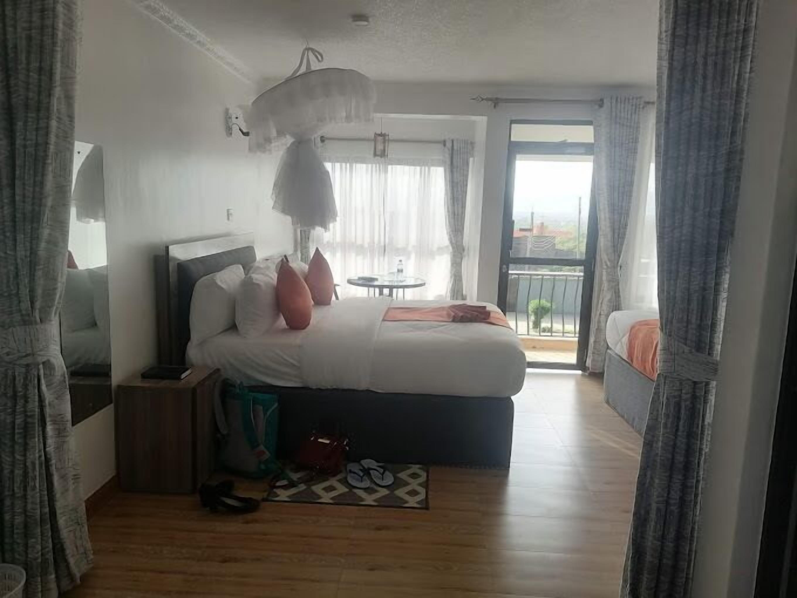 A bedroom with a large bed, a bedside table, a chair, a small table, and a balcony with a view.