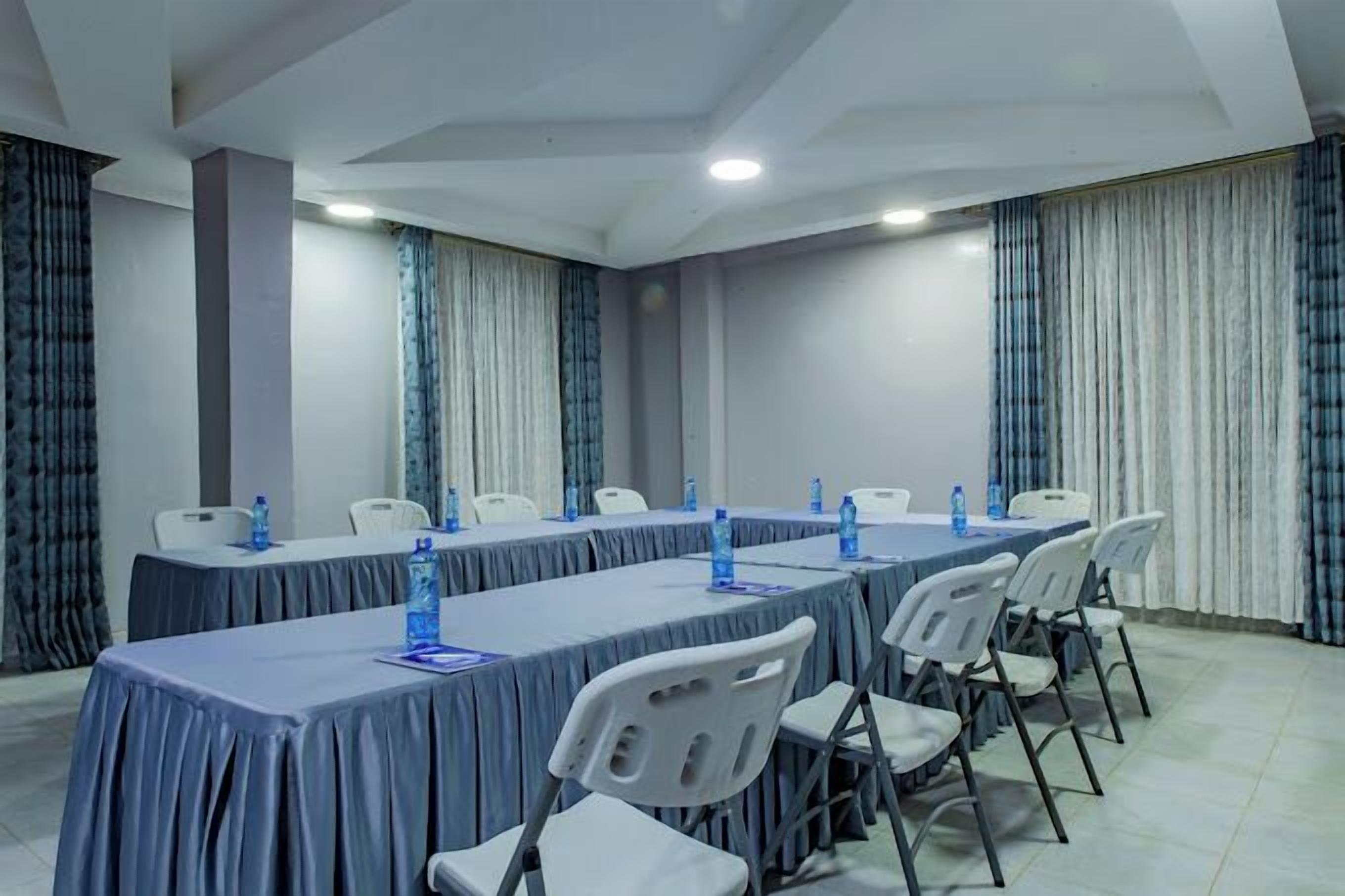Une salle de conférence avec une longue table, des chaises blanches et des bouteilles d’eau bleues.