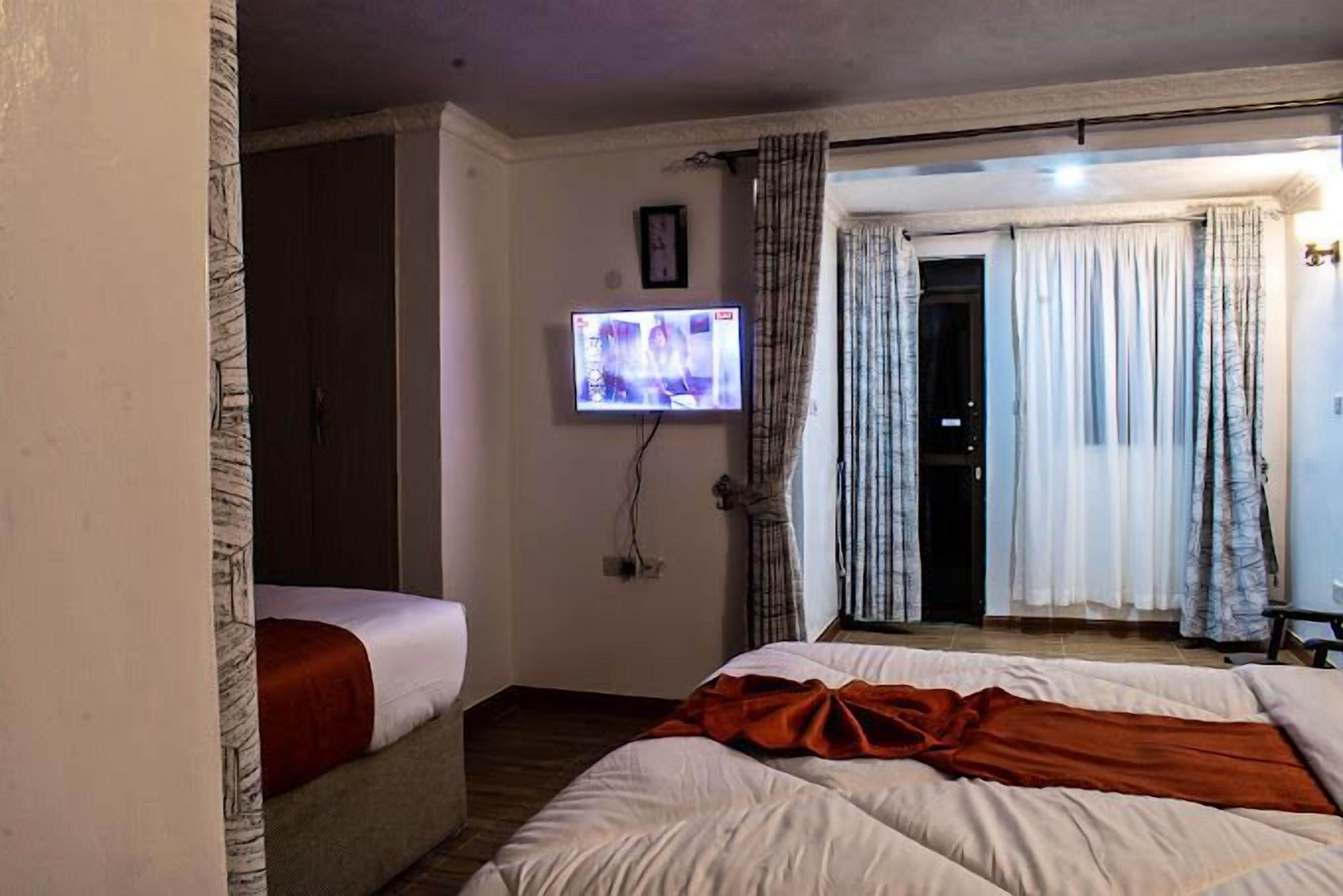 Een slaapkamer met een bed, een aan de muur bevestigde televisie en een deur die naar een andere kamer leidt.