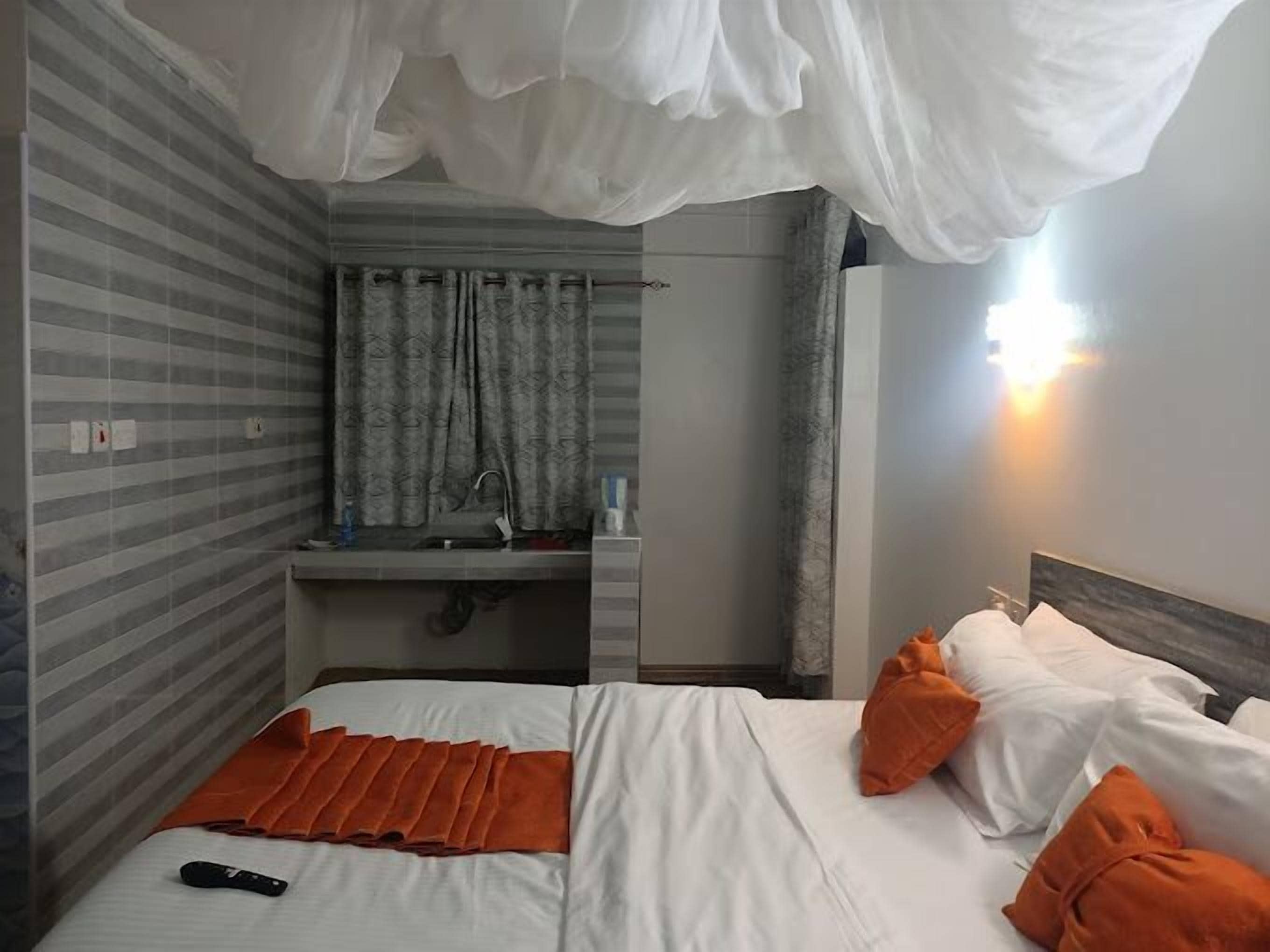 Habitación de hotel con cama, mesita de noche, espejo y baño visible a través de una puerta abierta.