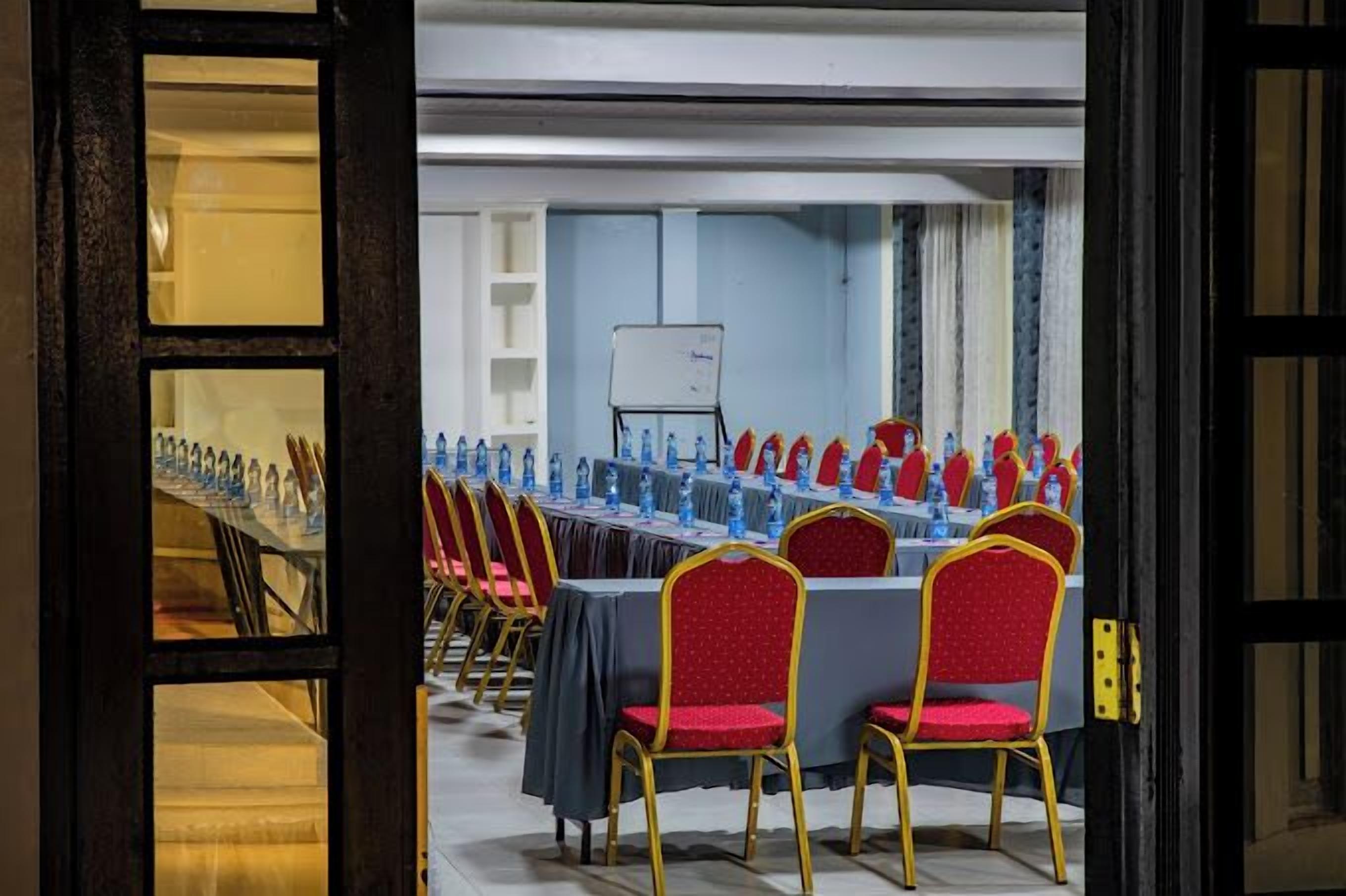 Une salle de conférence avec des rangées de tables et de chaises, un tableau blanc et des bouteilles d’eau.
