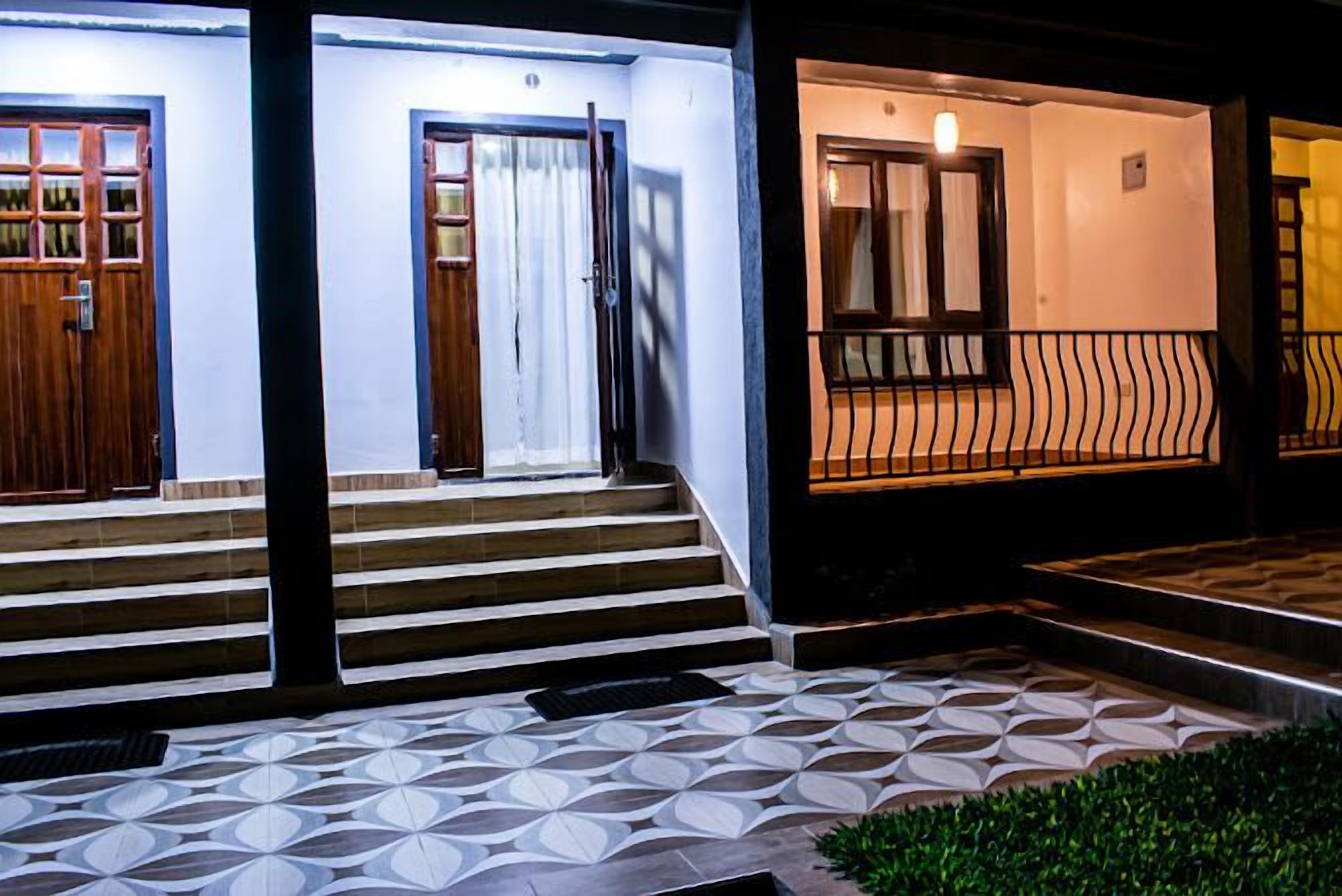 Un edificio con suelo de baldosas estampadas, puertas de madera y una escalera que lleva a un balcón con barandilla.