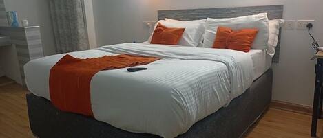 A neatly made bed with white and orange bedding, a dark headboard, and a wooden floor.