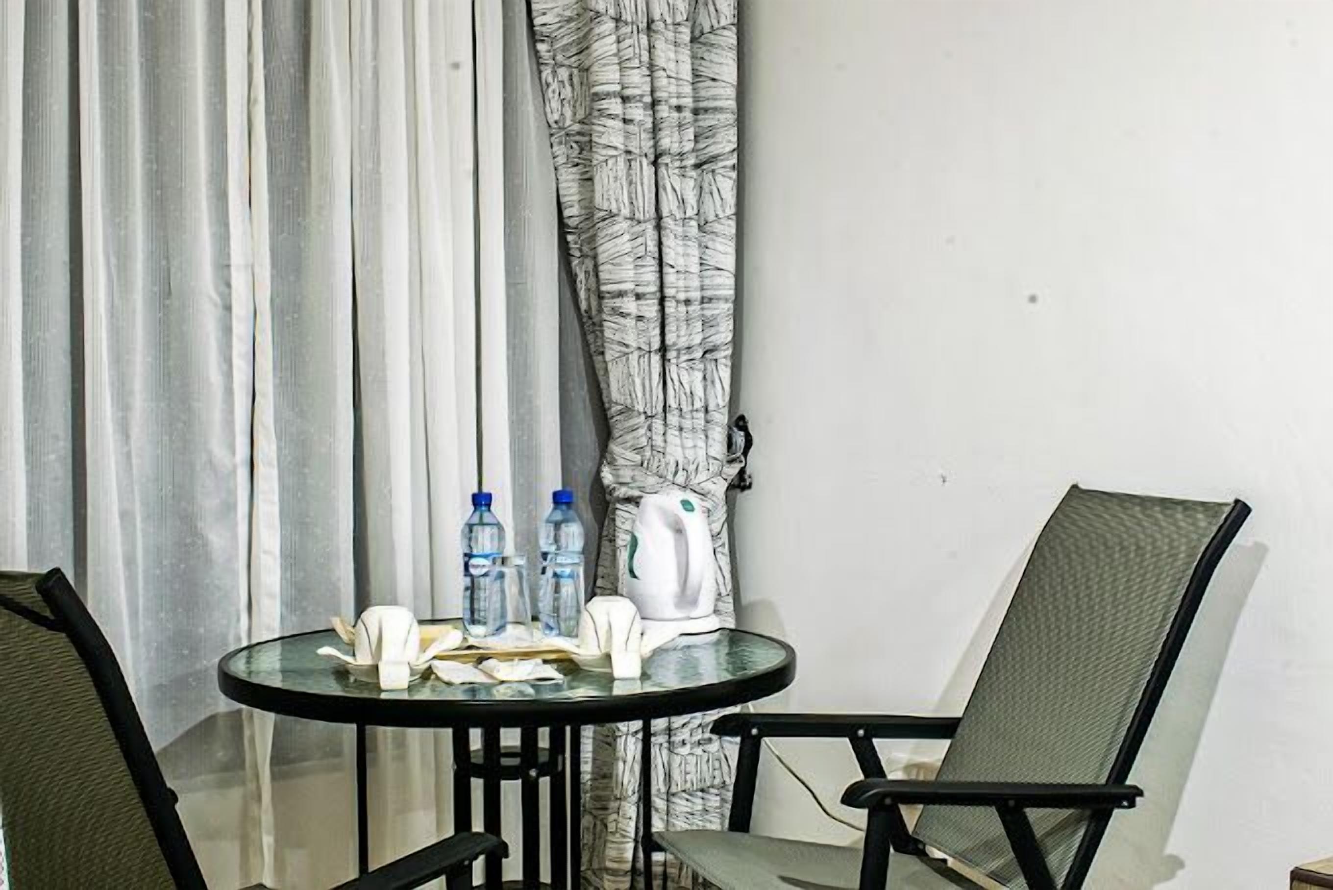 Une petite table ronde avec un plateau en verre, deux chaises, une bouilloire et des bouteilles d’eau.