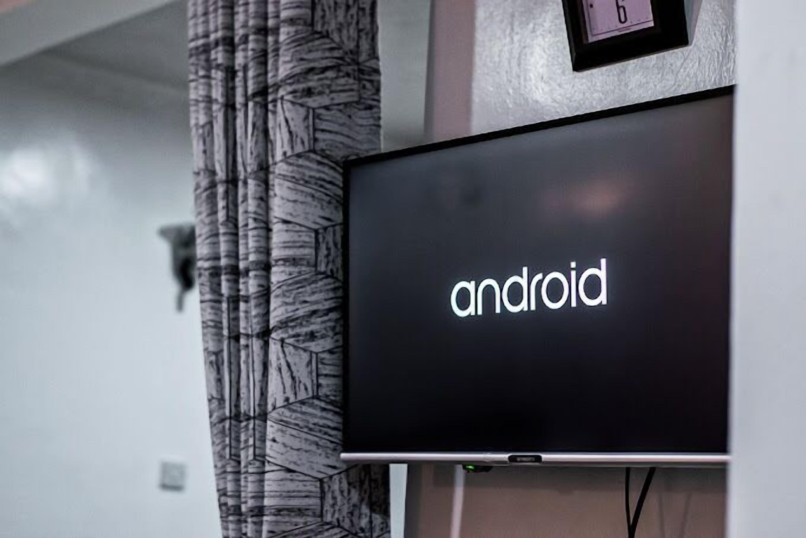 A black screen with the word "android" on it, mounted on a wall with a patterned curtain to the left.