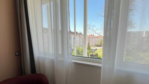 A room with a window, a red chair, and a view of buildings and trees outside. - Comfort Studio in a Premium Residence- Sport/cinema (Huningue)
