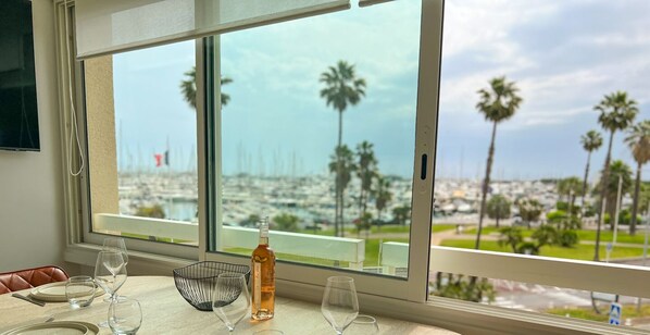 A dining table with a bottle of wine and wine glasses, overlooking a marina with palm trees. - LE PORT VAUBAN Harbor view for 4 by Sunset (Antibes)