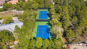 Vista aérea de un complejo de canchas de tenis rodeado de árboles frondosos, con un edificio al lado izquierdo.