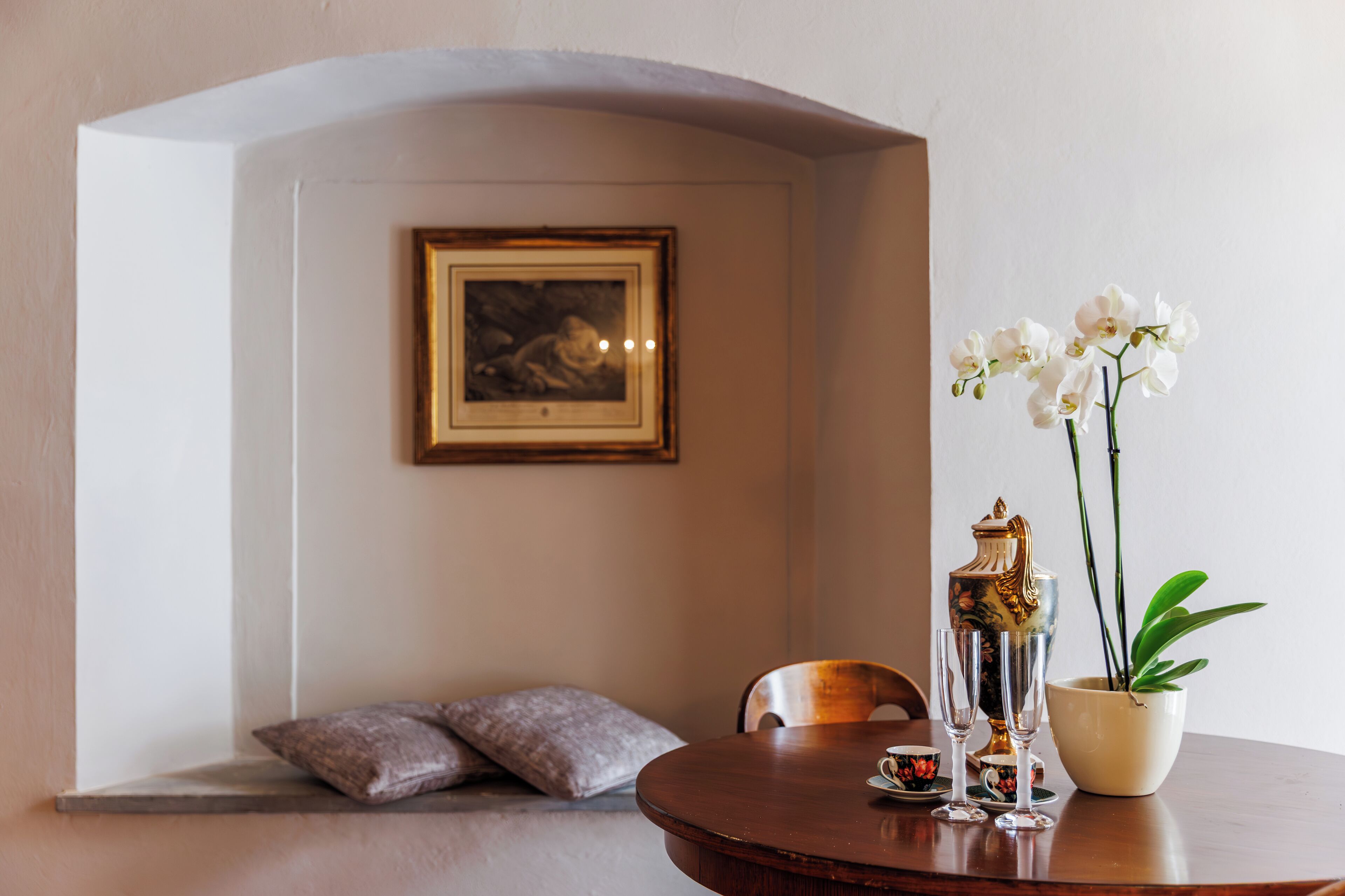 Een eetgedeelte met een ronde tafel, een lijst met foto, een vaas met witte bloemen en een decoratieve urn.