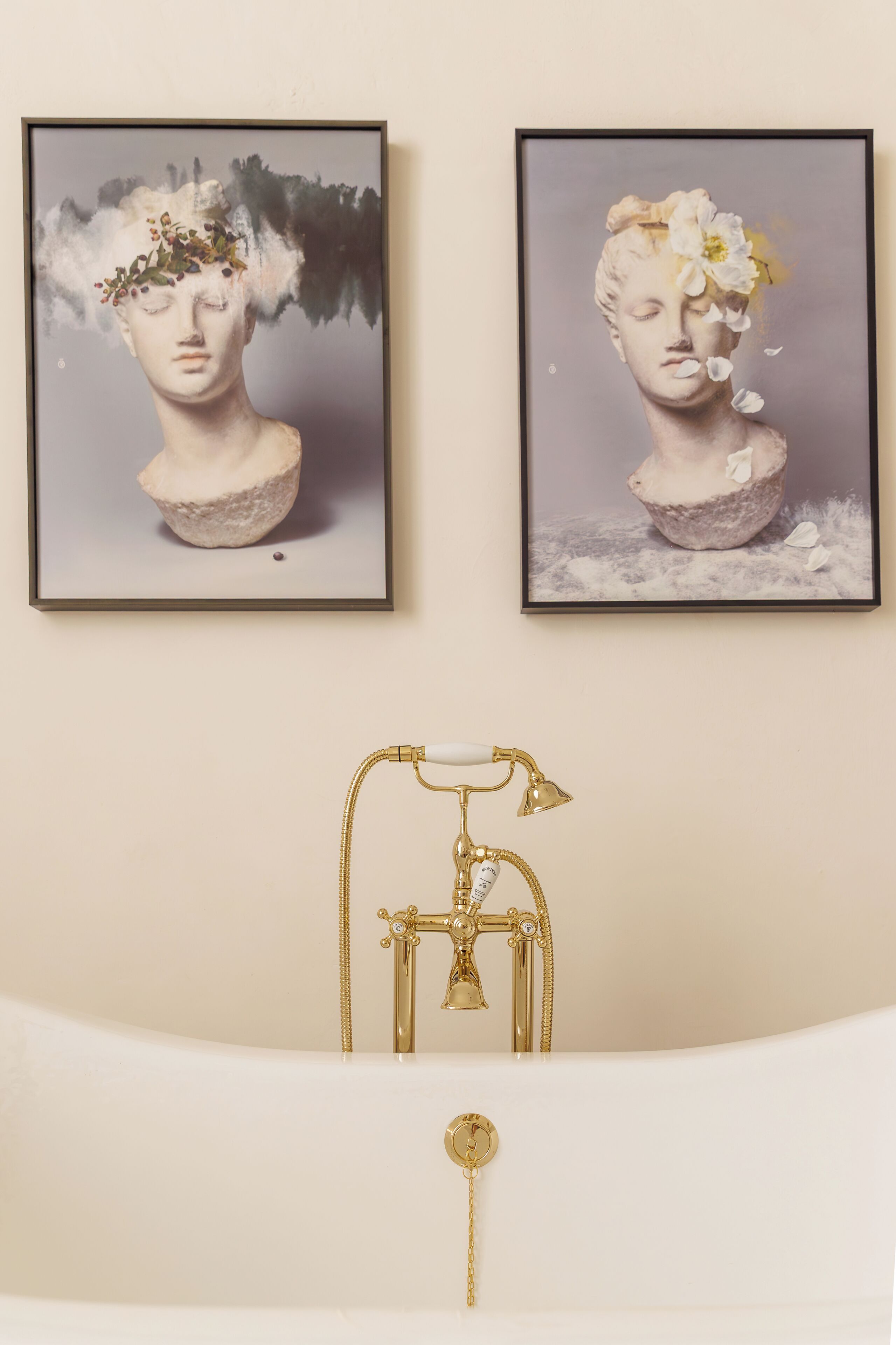 Two framed artworks above a bathtub with a vintage faucet.