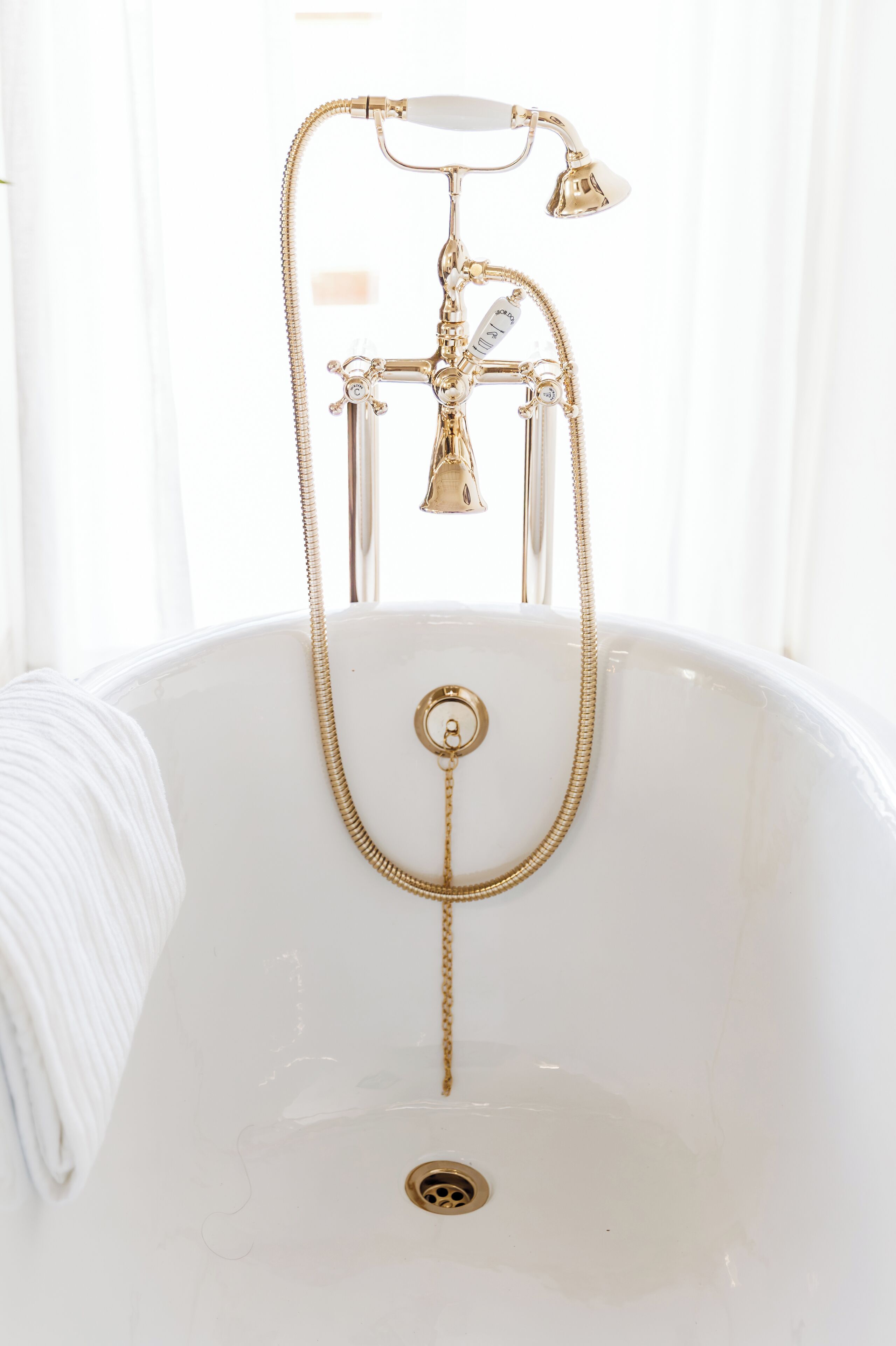 A white bathtub with a gold faucet and showerhead, a gold chain, and a drain.