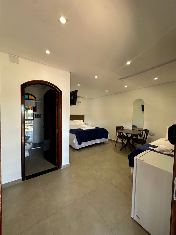 Habitación de hotel con dos camas, un escritorio, una silla, una mesita, un espejo y un baño visible a través de un arco.