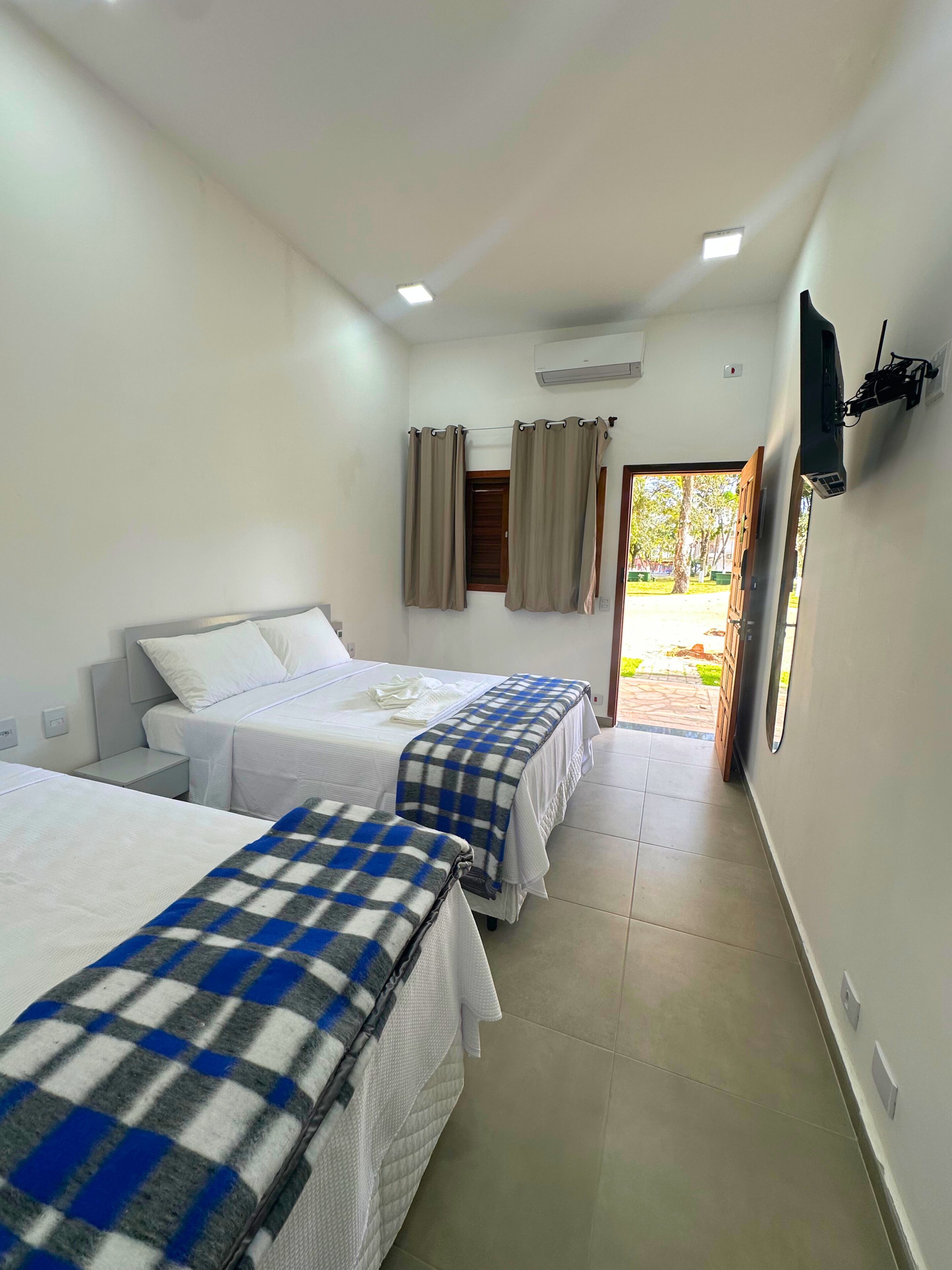 A hotel room with two beds, a TV mounted on the wall, and a window with curtains.