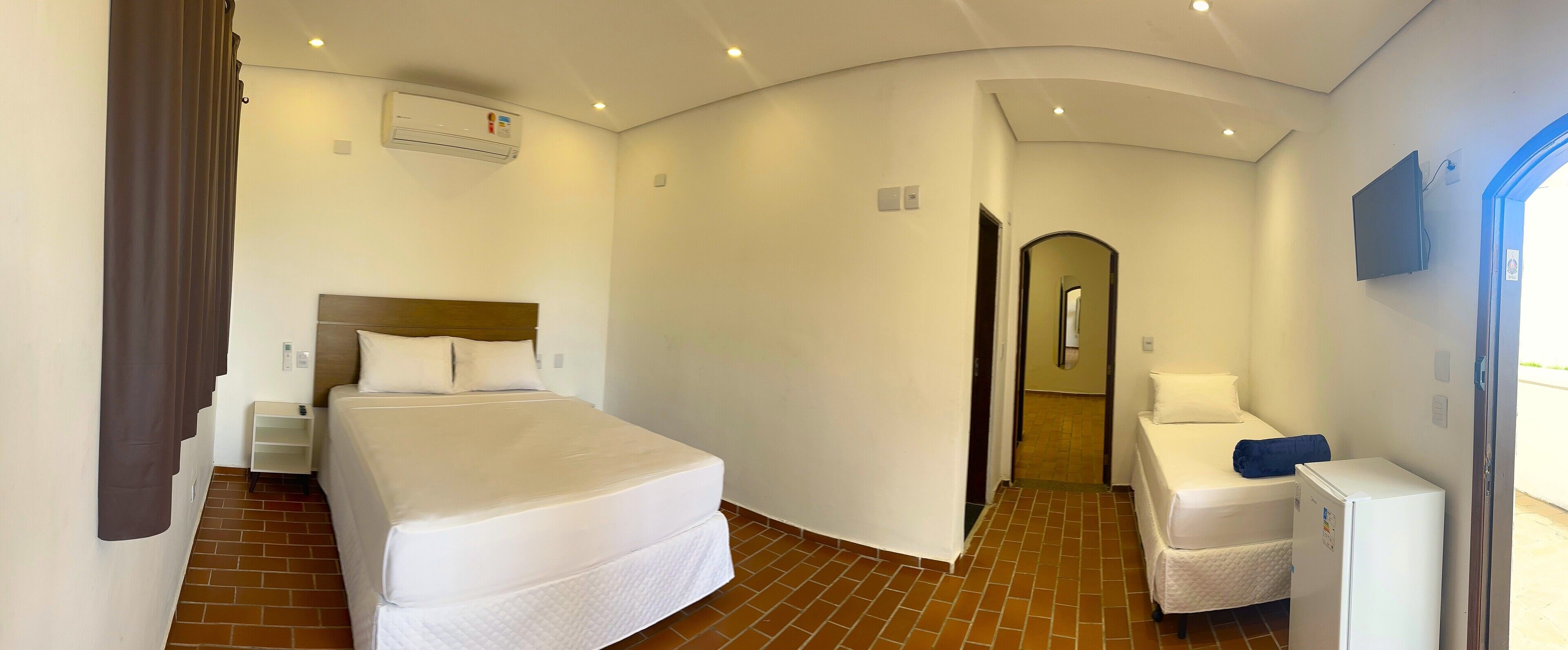 Habitación de hotel con una cama grande, una cama individual, un escritorio, una silla, un refrigerador y un baño con espejo.