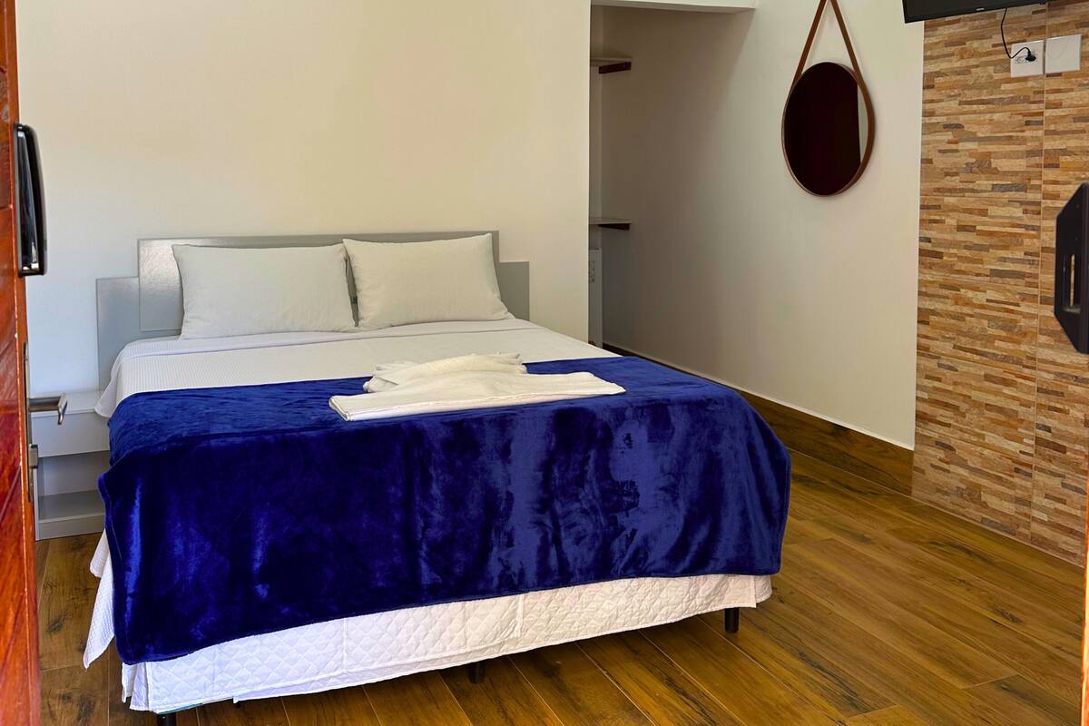 Una habitación de hotel moderna con una cama grande, suelo de madera, televisor montado y equipo de aire acondicionado.