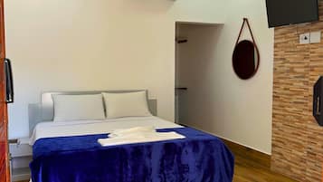 A modern hotel room with a large bed, wooden flooring, a mounted TV, and an air conditioning unit.