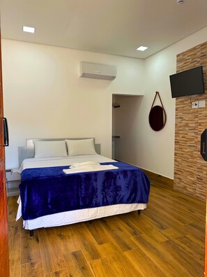 Una habitación de hotel moderna con una cama grande, suelo de madera, televisor montado y equipo de aire acondicionado.
