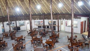 Un restaurant doté d’un toit de chaume élevé, de tables et de chaises en bois, et d’un comptoir central.