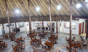 Un restaurante con un techo alto de paja, mesas y sillas de madera, y una barra central.