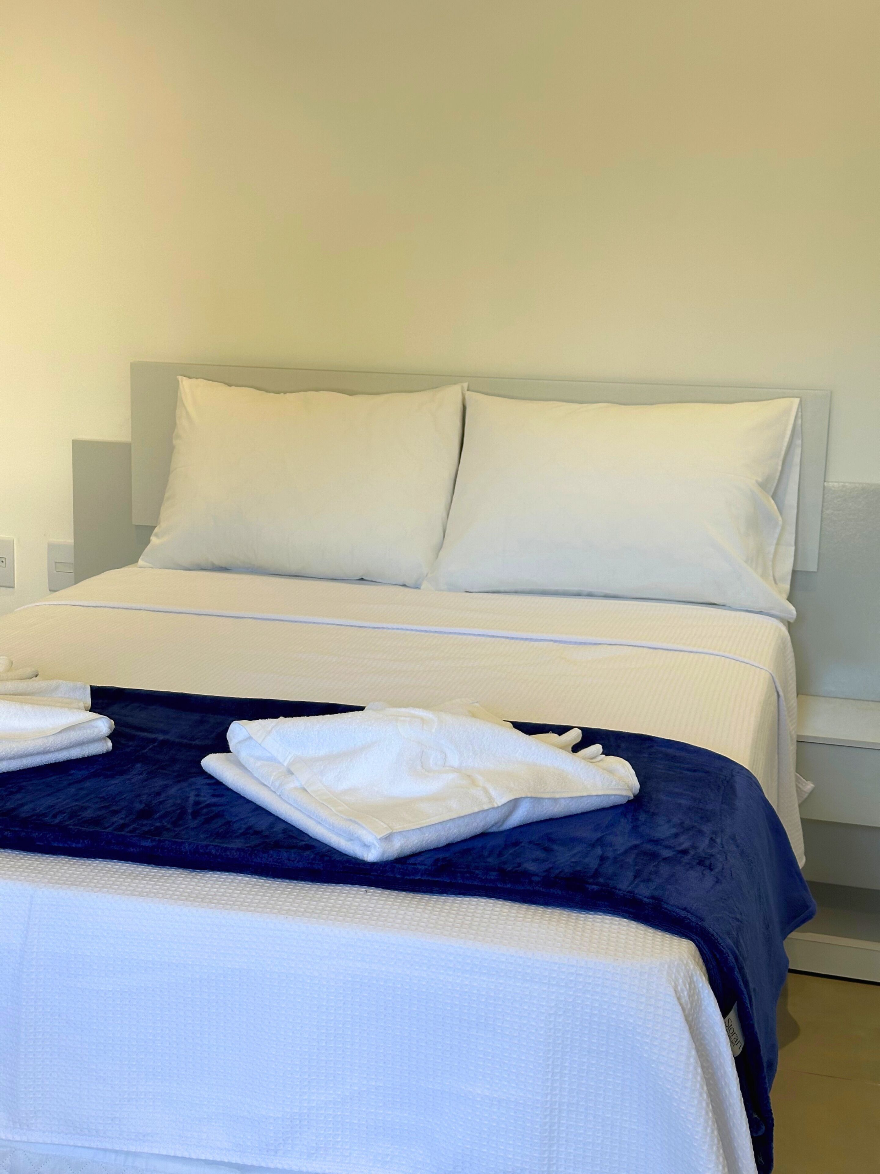 A neatly made bed with white linens and a dark blue bedspread, accompanied by folded white towels.