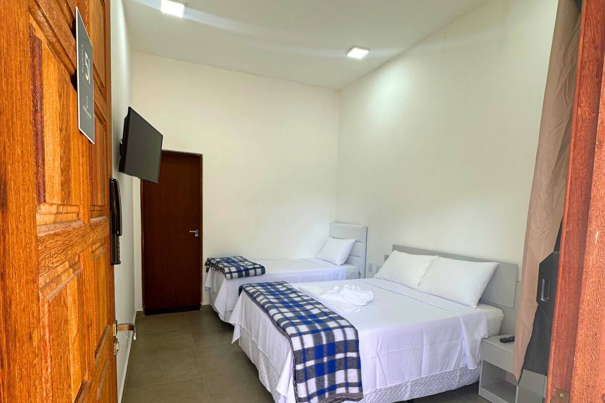 Habitaci ón de hotel con dos camas, un televisor montado en la pared y una puerta de madera.
