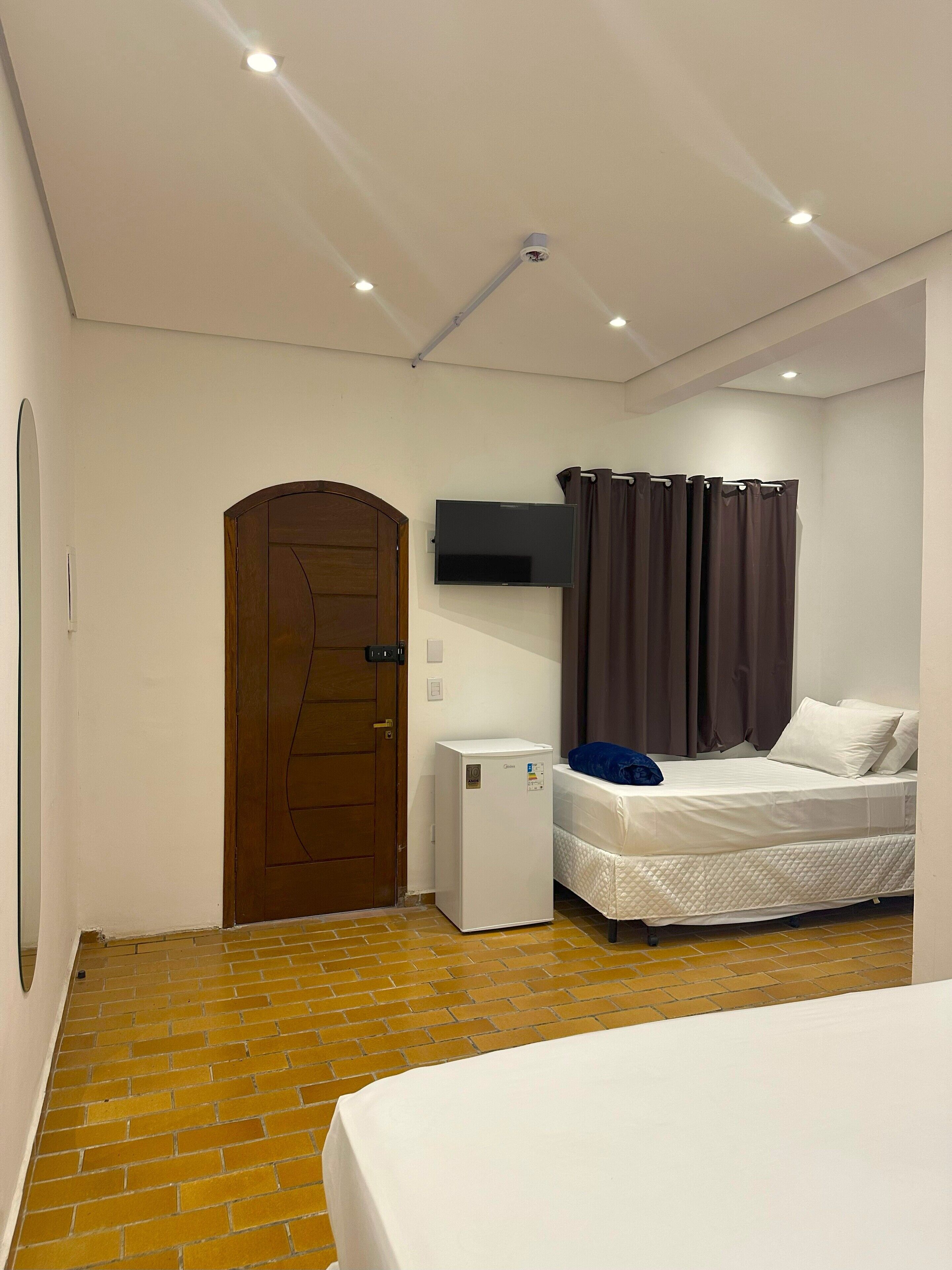 Un dormitorio con cama, un refrigerador pequeño, un televisor montado en la pared y una puerta.