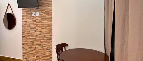 Una habitación con una mesa redonda de madera, dos sillas de madera, un televisor de pantalla plana montado en una pared con diseño de ladrillos y un bolso colgando.