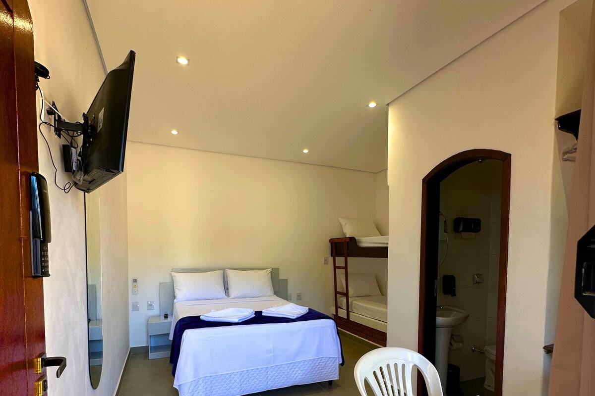 Habitación de hotel compacta con una cama individual, una mesita pequeña y un televisor fijado a la pared.