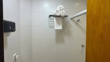 Un baño pequeño y funcional con inodoro, toallero con toallas enrolladas, dispensador de jabón y zona de ducha.