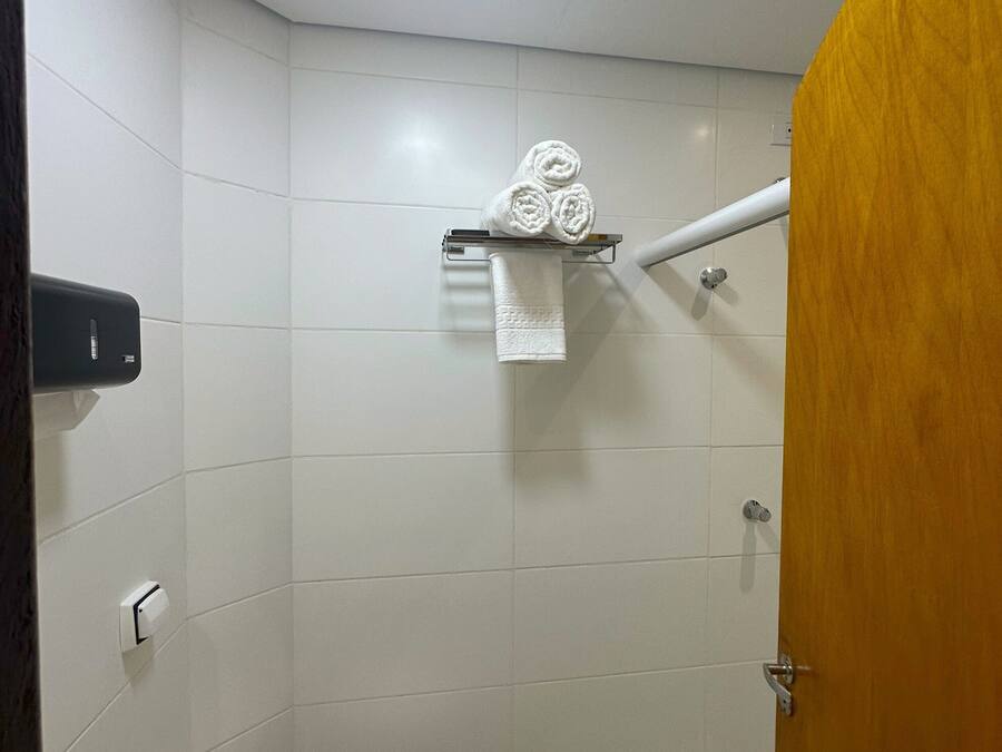 Un baño pequeño y funcional con inodoro, toallero con toallas enrolladas, dispensador de jabón y zona de ducha.