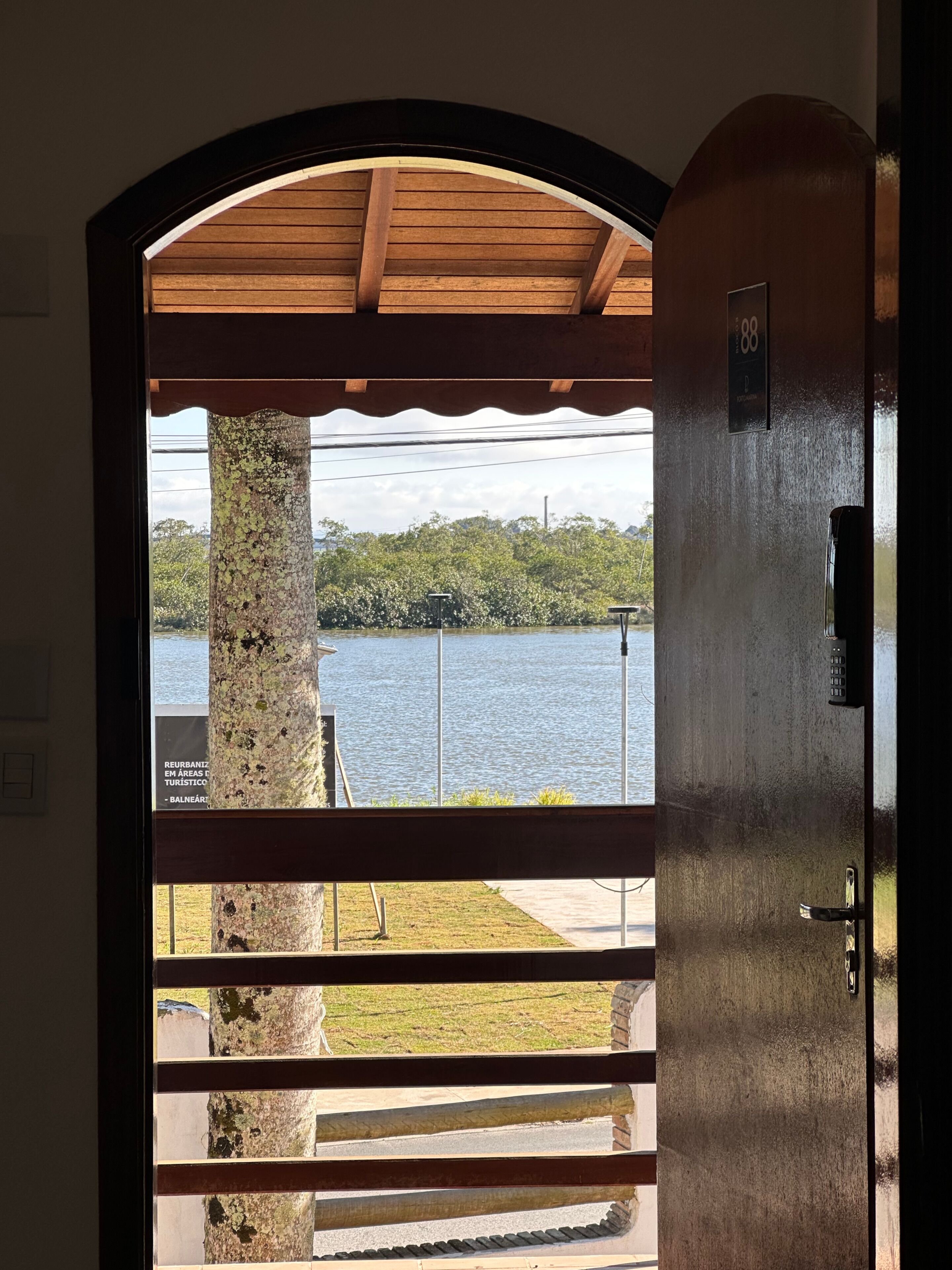 Puerta que da a un balcón con vista a un lago y árboles.
