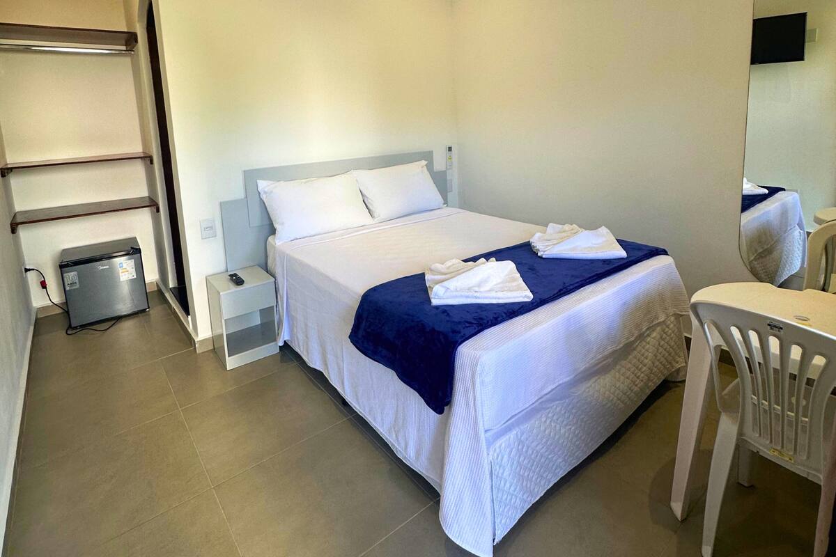 Habitación de hotel con cama, escritorio, silla, refrigerador pequeño y espejo.