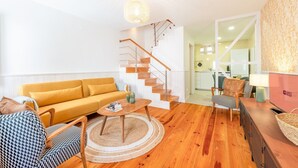A modern living room with a yellow sofa, a wooden coffee table, a staircase, and a kitchen in the background. - GuestReady - Beautiful stay in Seixal (Seixal)