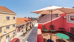 A narrow street with buildings on either side, outdoor seating with umbrellas, and a red and white tiled roof. - GuestReady - Beautiful stay in Seixal (Seixal)