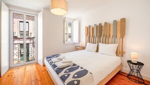 A bedroom with a bed, wooden headboard, bedside tables, and a view of the outside balcony. - GuestReady - Beautiful stay in Seixal (Seixal)