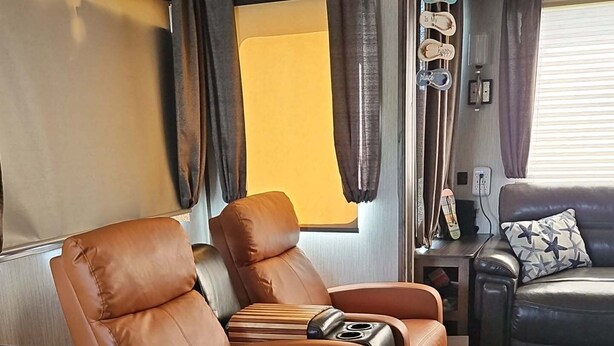 Un salon chaleureux avec un canapé en cuir marron, une chaise en bois et une petite table sur laquelle repose une guitare.