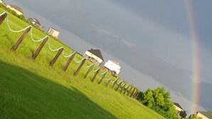 Un champ verdoyant avec un arc-en-ciel, une clôture en bois et des maisons en arrière-plan.