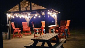 Un espace extérieur abrité, doté de tables et de chaises en bois, éclairé par des guirlandes lumineuses.