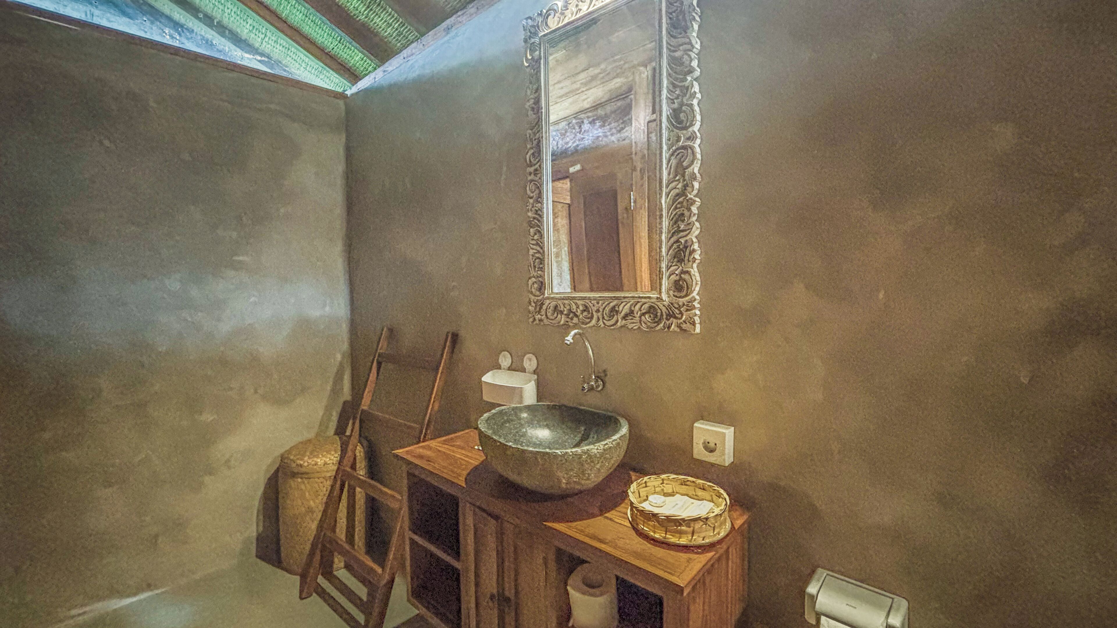 A bathroom with a stone sink, wooden vanity, and a mirror with an ornate frame.