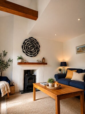 Una sala de estar con chimenea, un sofá azul, una mesa de centro de madera y una obra de arte abstracta colgada en la pared.
