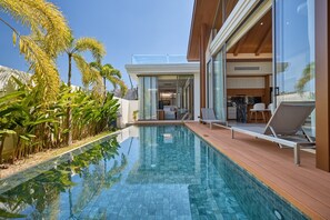 A modern pool area with clear blue water, wooden deck, and lounge chairs.