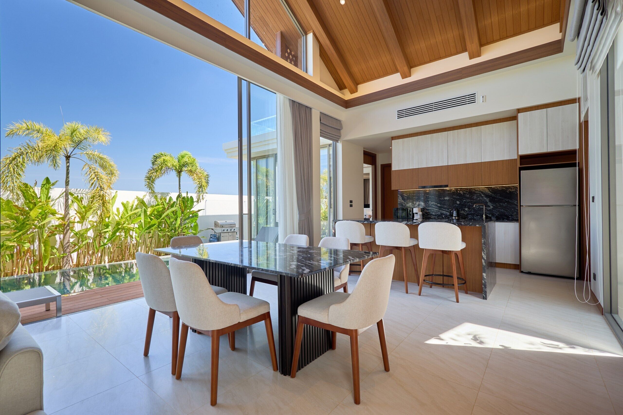 A modern kitchen with a large island, white chairs, and a view of palm trees.