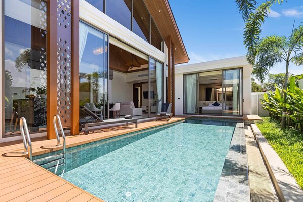 A modern pool area with a wooden deck, glass doors leading to a living area, and a clear blue pool. - Bangtao Ozon Villas by My Home Phuket (Choeng Thale)