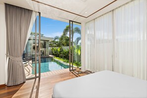 A modern bedroom with a large bed, a glass door leading to a pool, and a view of greenery. - Bangtao Ozon Villas by My Home Phuket (Choeng Thale)